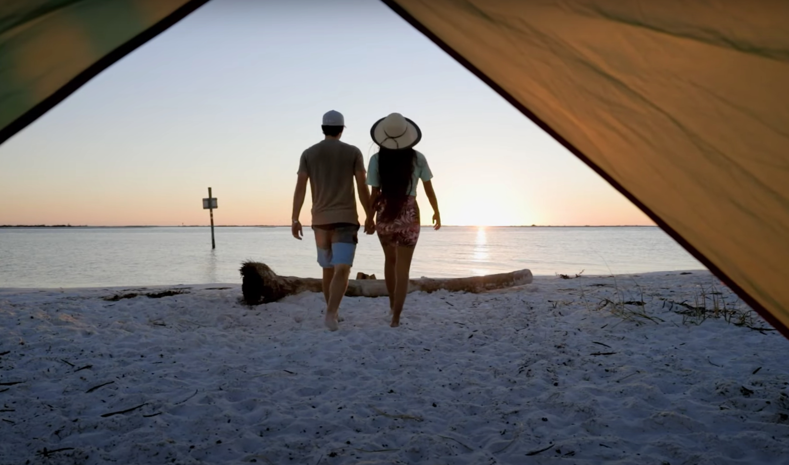A couple walks away from a tent toward the water at Shell Key during sunset