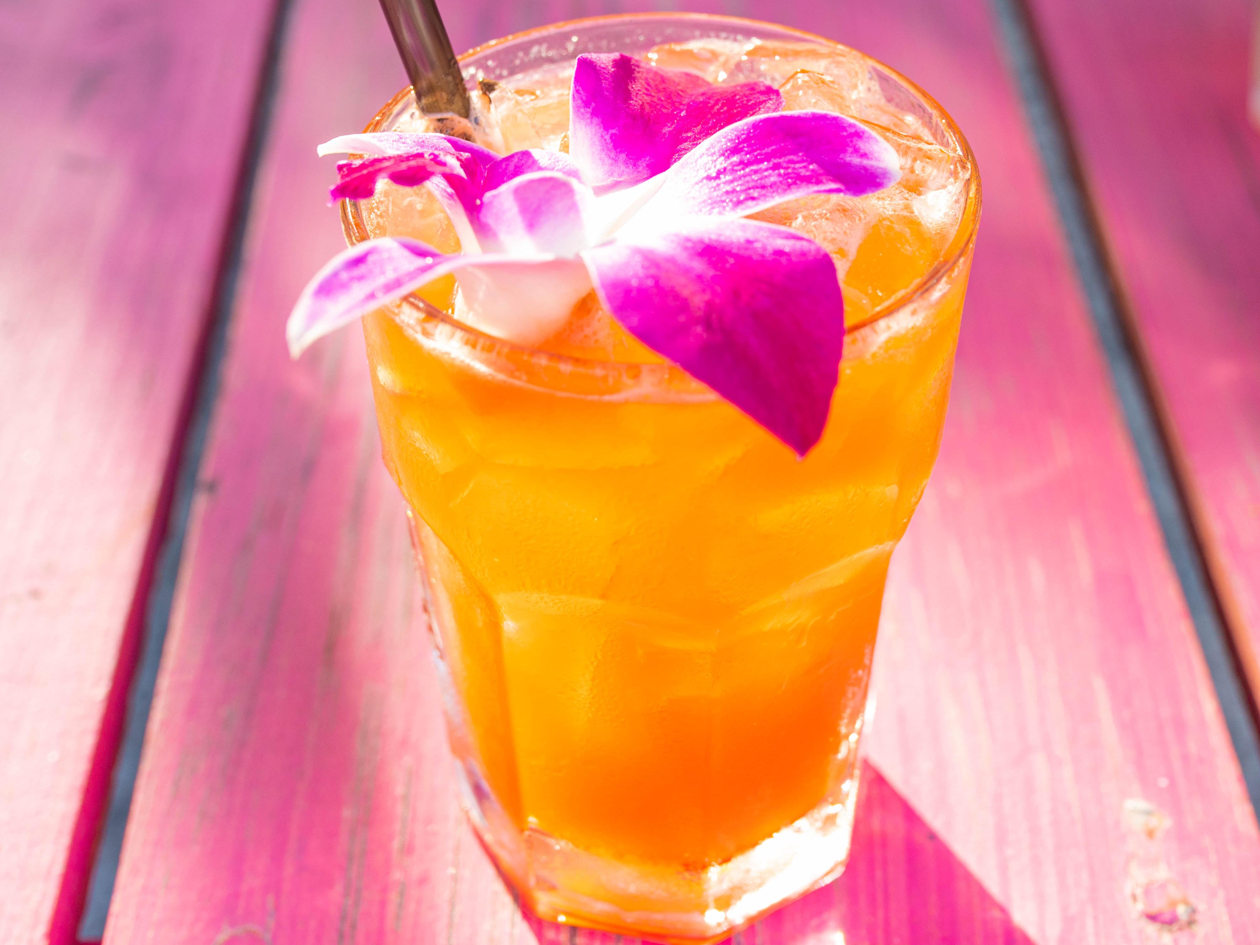 a fruity drink in a tall glass with a pink and white orchid and a straw on a pink table at Mullet's Fish Camp