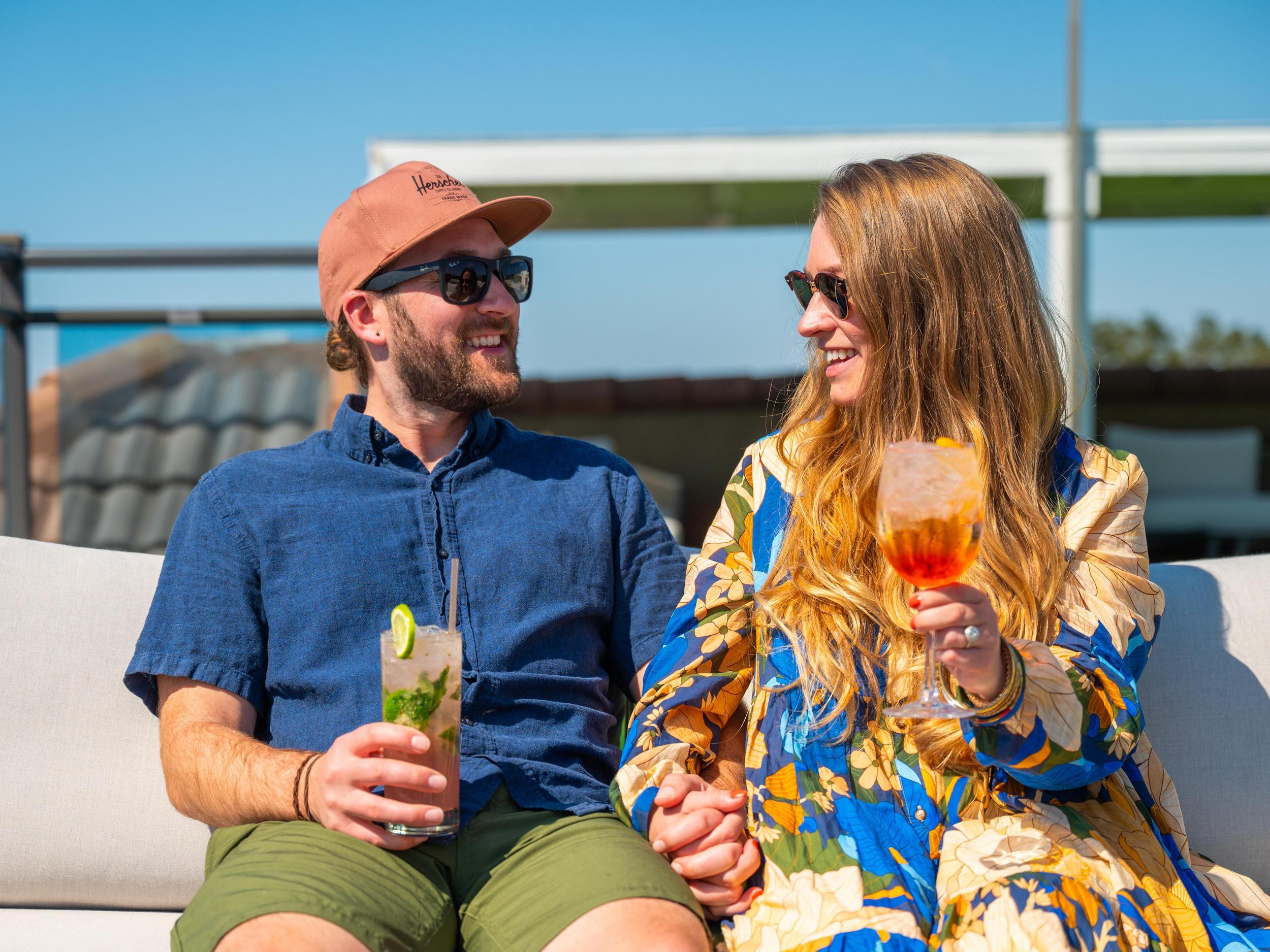 a couple smiles and holds hands and tropical drinks on the rooftop of Hotel Zamora