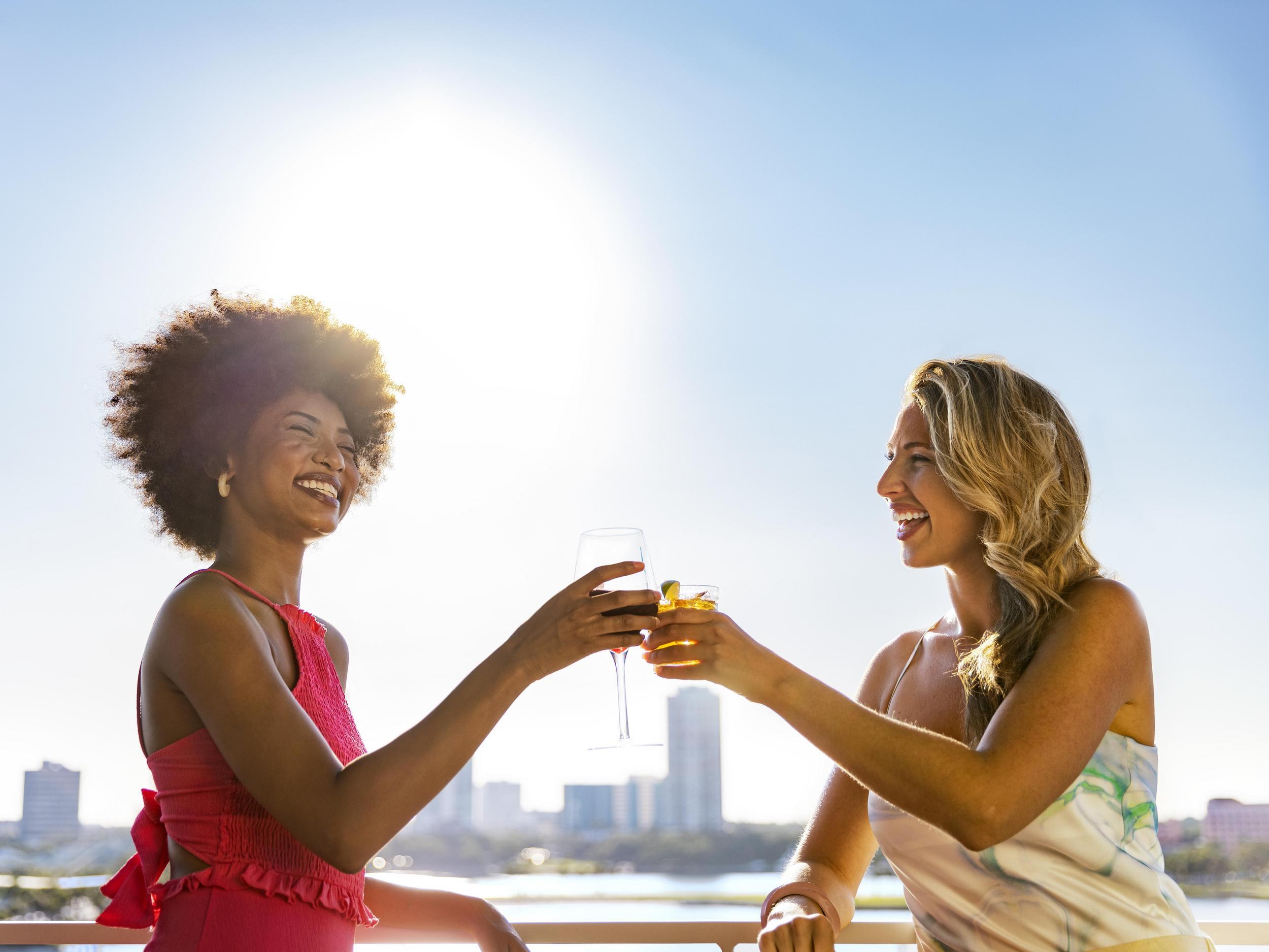 two women toast with cocktails at Pier Teaki rooftop bar at the St. Pete Pier