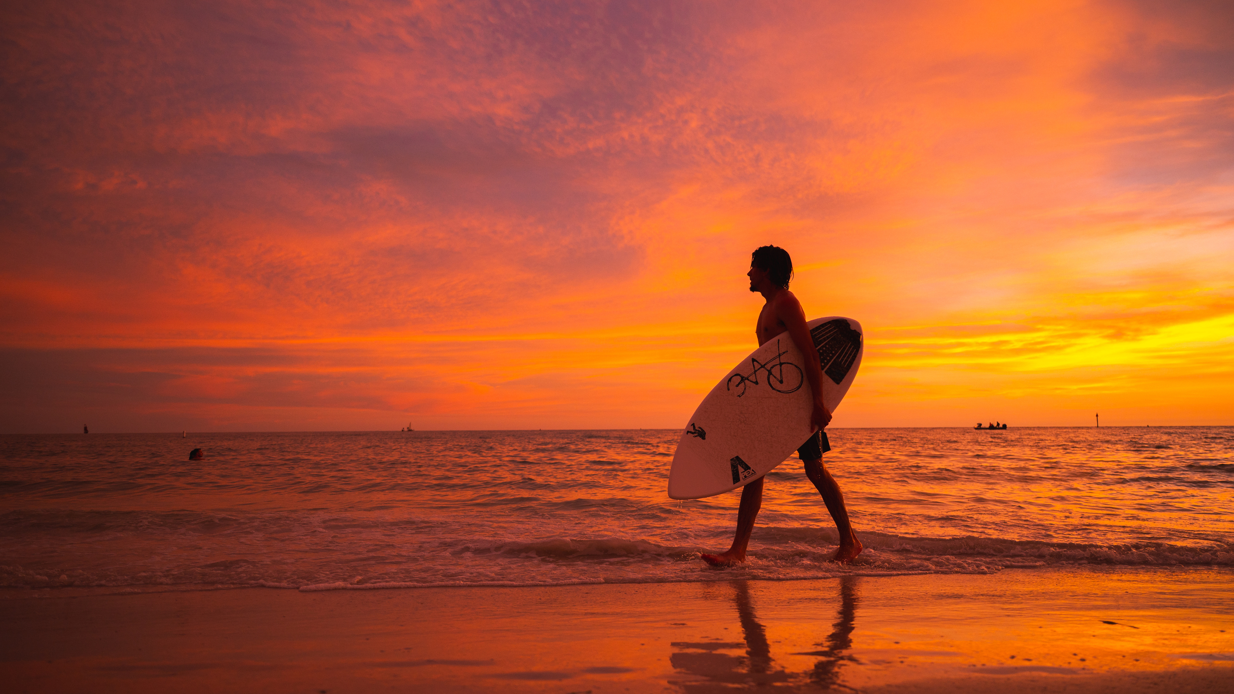 a man with a surfboard walks along the water's edge in Treasure Island at sunset