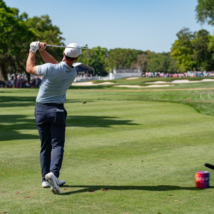 A golfer right after hitting the ball. A large crowd can be seen at a distance.
