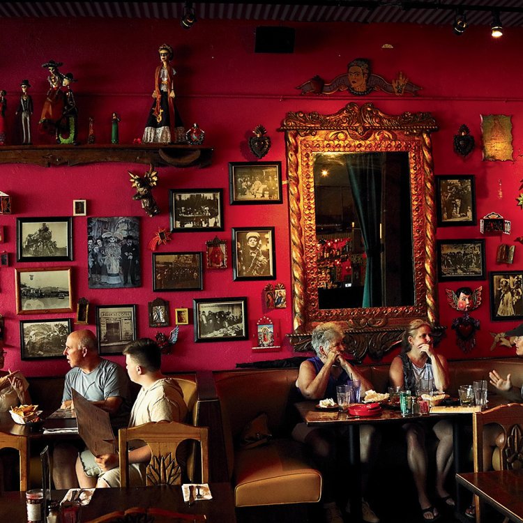 Six dinners eating at Casa Tina restaurant in Dunedin. The wall is red and decorated with multiple portraits.