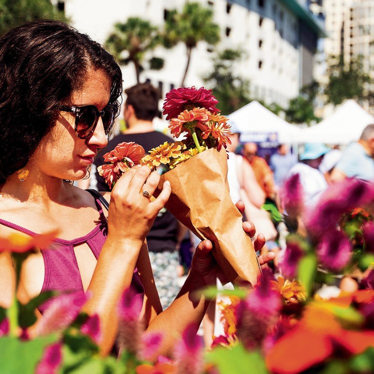 A young lady wearing sunglasses smelling flowers on display.