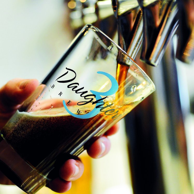 A person pouring dark beer in a 3 Daughters Brewery glass.