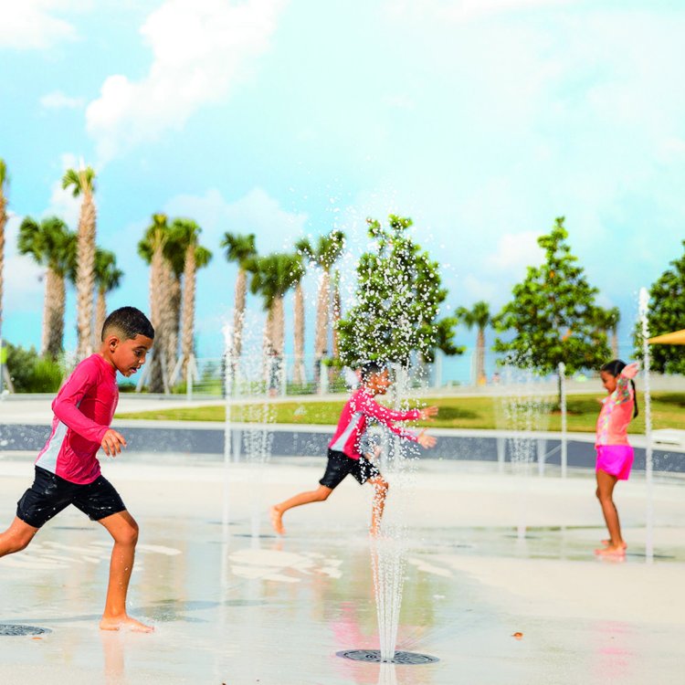 Three children play at the splash pad at St. Pete Pier with palm trees in the background