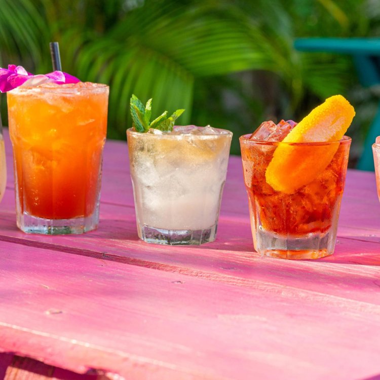 5 tropische Cocktails, garniert mit Früchten auf einem rosa Tisch im Freien