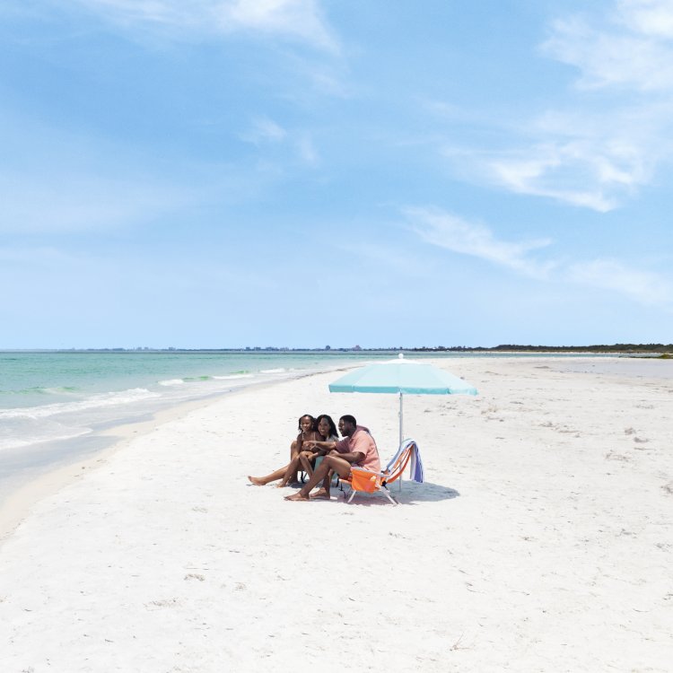 a mom, dad and little girl sit under a beach umbrella at Fort De Soto Park's beautiful white-sand beach
