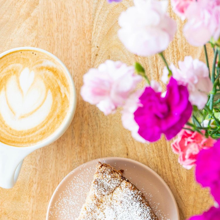 latte in a ceramic mug with a pastry and bright pink flowers