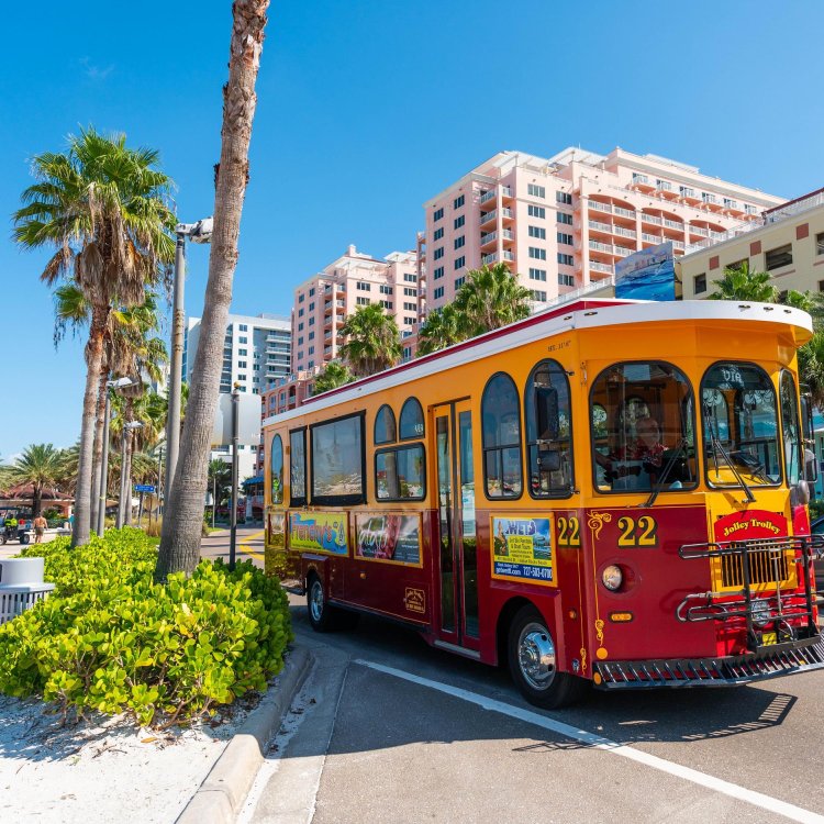 a bright red and yellow trolley on a roadway with palm trees and a pink building nearby