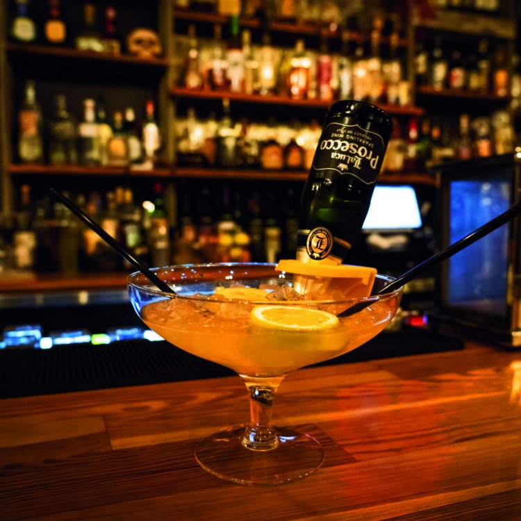 A photo of a pink cocktail with two straws on a bar