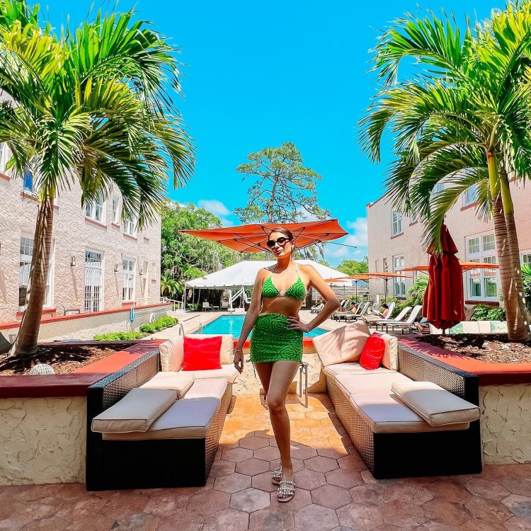 a woman in a bright green bathing suit posing in front of benches and a pool near palm trees at the Fenway Hotel