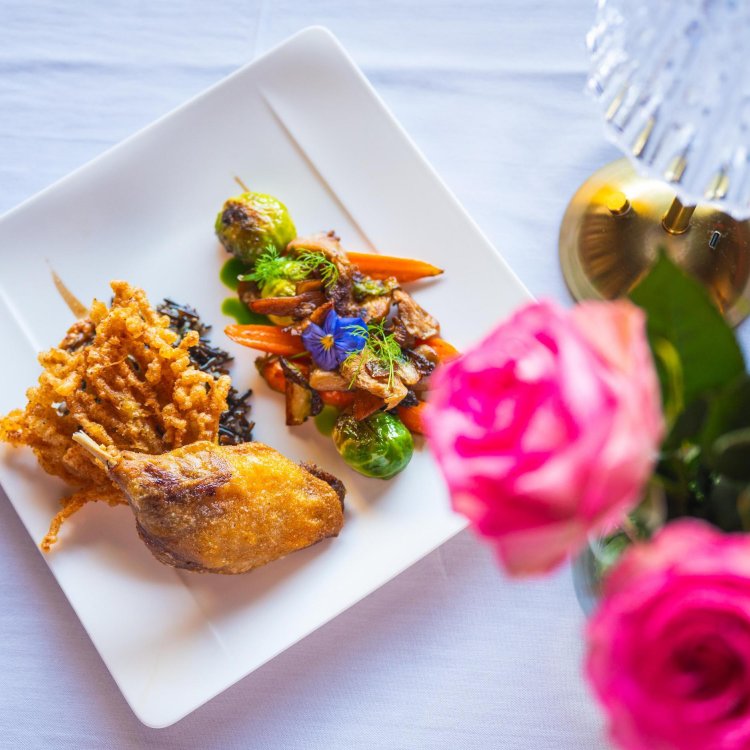 A view of a beautifully plated dish at Black Pearl Restaurant in Dunedin, accompanied by bright pink roses on the white linen tablecloth