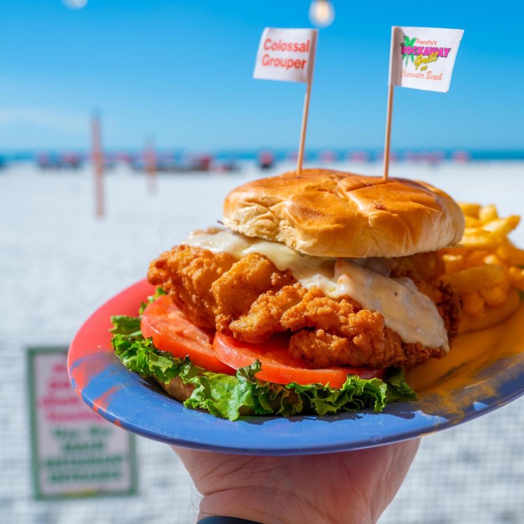 a person holding a plate with a fried grouper sandwich at Frenchy's Rockaway Grill, with a view of Clearwater Beach