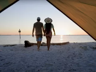 A couple walks away from a tent toward the water at Shell Key during sunset