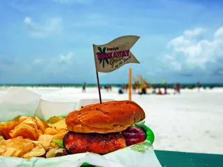 A grouper sandwich with fries at an outdoor patio with a view to the beach. Beach goers can be seen at a distance.