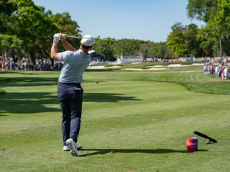 A golfer right after hitting the ball. A large crowd can be seen at a distance.