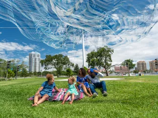 A family enjoying themselves in the grass field under the Echelman Sculpture at the St. Pete Pier.