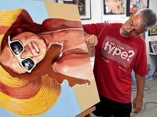 Painter Bob Ribits working at Soft Water Studios in the Warehouse Arts District finishing a painting of a lady in swimsuit, sunglasses and beach hat.