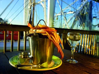 A bucket of crab legs and a glass of white wine over an outdoor table from the Rusty Bellies Restaurant