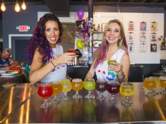 Two servers hold up a beer in front of more beer at Hawthorne Bottle Shop