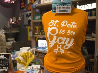 A close view of an orange t-shirt that says "St. Pete is so Gay". Other merchandise and souvenirs are at display.