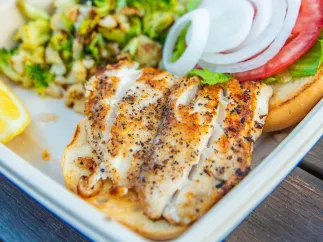 A close view of a grouper fish plate with onions, tomatoes and green vegetables.