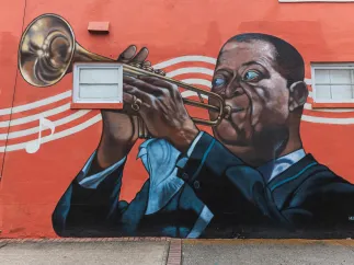 A mural by Herbert Davis in South St. Pete on a red background depicts Louis Armstrong playing the trumpet