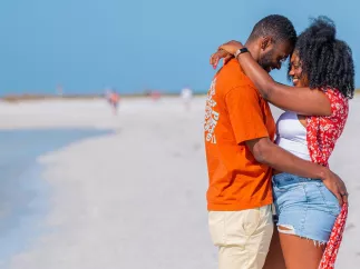 Couple snuggles while standing on a white-sand beach