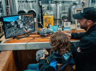 A man and boy play an old-style videogame inside a brewery.
