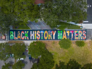 a drone view of a multicolored black history matters mural in block letters on a road near trees