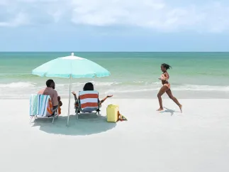 Girl running on the beach toward parents under an umbrella