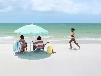 Girl running on the beach toward parents under an umbrella
