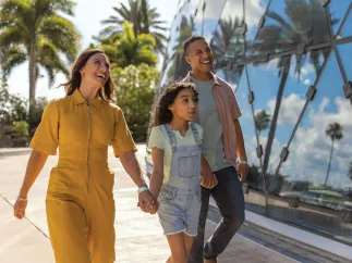 a mother and father hold hands with a little girl while walking outside the dali museum