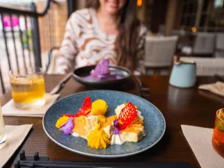 a colorful plate of food with cocktail surrounding it and a young woman in the background at Fortu restaurant