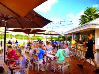 a busy outdoor deck at a restaurant on the water with diners and a server