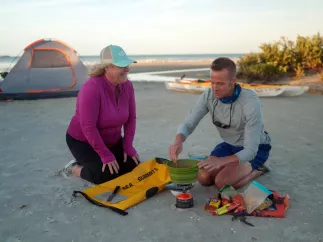 man and woman cooking food on the beach