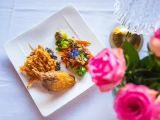A view of a beautifully plated dish at Black Pearl Restaurant in Dunedin, accompanied by bright pink roses on the white linen tablecloth