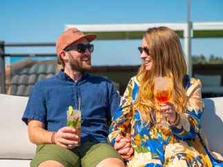 a couple smiles and holds hands and tropical drinks on the rooftop of Hotel Zamora