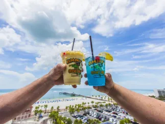 two tropical drink in a Jimmys Crow's Nest plastic cup cheersing with rooftop view in background of Clearwater Beach and Pier