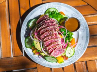 a fresh green salad with thin slices of raw ahi tuna decorated with sesame seeds on a blue and white china plate
