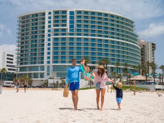 a mom, dad and two kids smile while walking out onto the beach at Opal Sands Resort