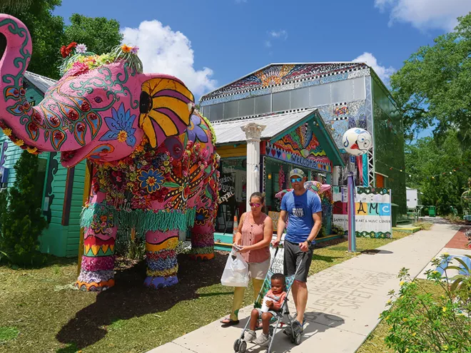 A couple strolling with a child in front of the pink elephant in front of the Safety Harbor Art & Music Center