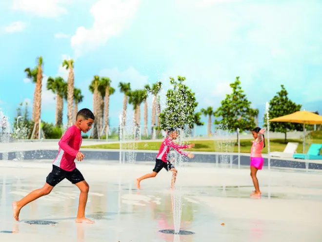 Three children play at the splash pad at St. Pete Pier with palm trees in the background