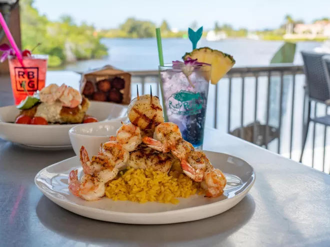 Two seafood dishes and two drinks on a bar overlooking the water at Rusty Bellies.