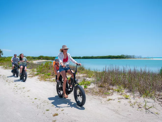 Family on ebikes rides along a sandy path by the water
