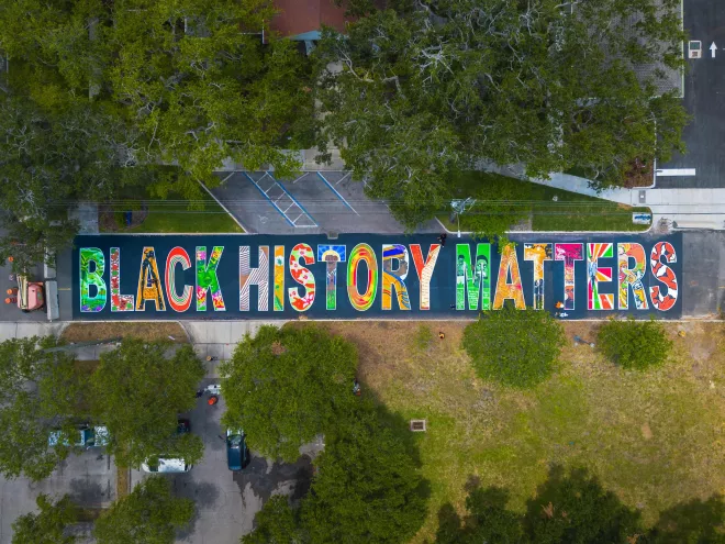 a drone view of a multicolored black history matters mural in block letters on a road near trees