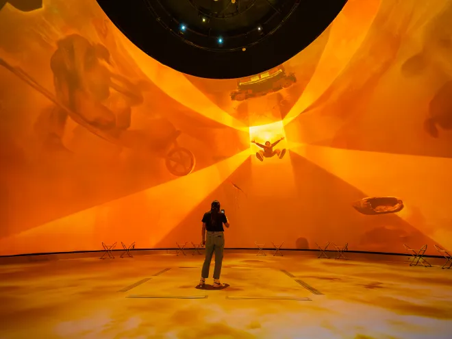 projection in a dome, bright orange, with a woman in front of it 