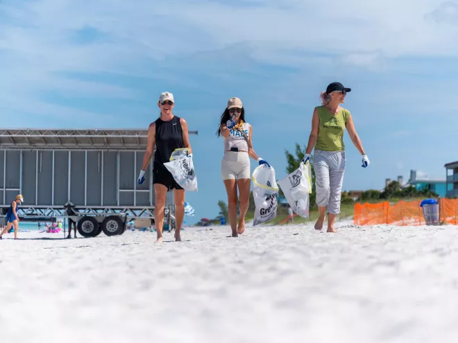 three women with trash bags at a beach clean up