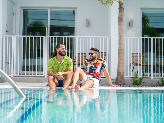 two smiling men in colorful shirts sit with their feet in the pool at Mint House